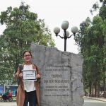 Ngoc holds her UGRAD Post by her home university sign, an engraved stone