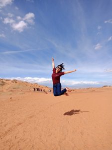 Huong jumps with the blue sky above her and sandstone below her