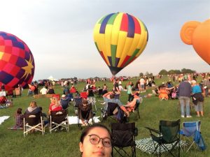 Migma takes a selfie as a hot air balloon lifts off behind her