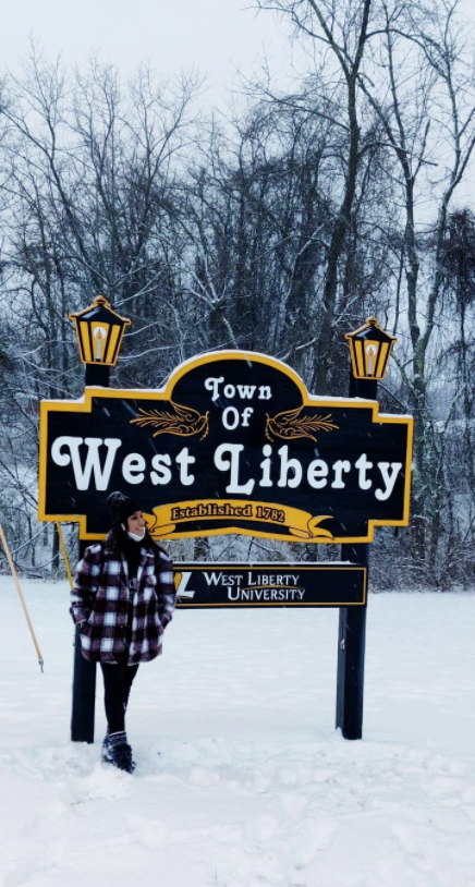 Student stands in front of the "Town of West Liberty" sign.