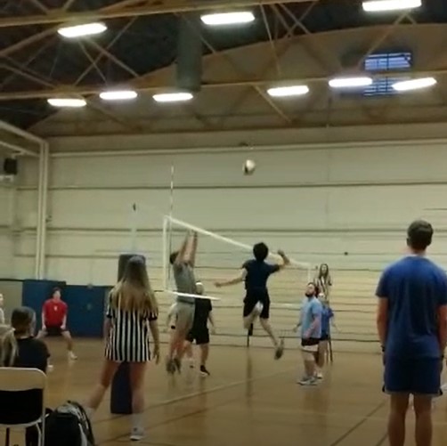 A person jumps to spike a volleyball across the net