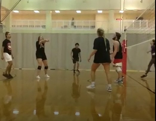 A volleyball team with one person raising their arms to hit the ball